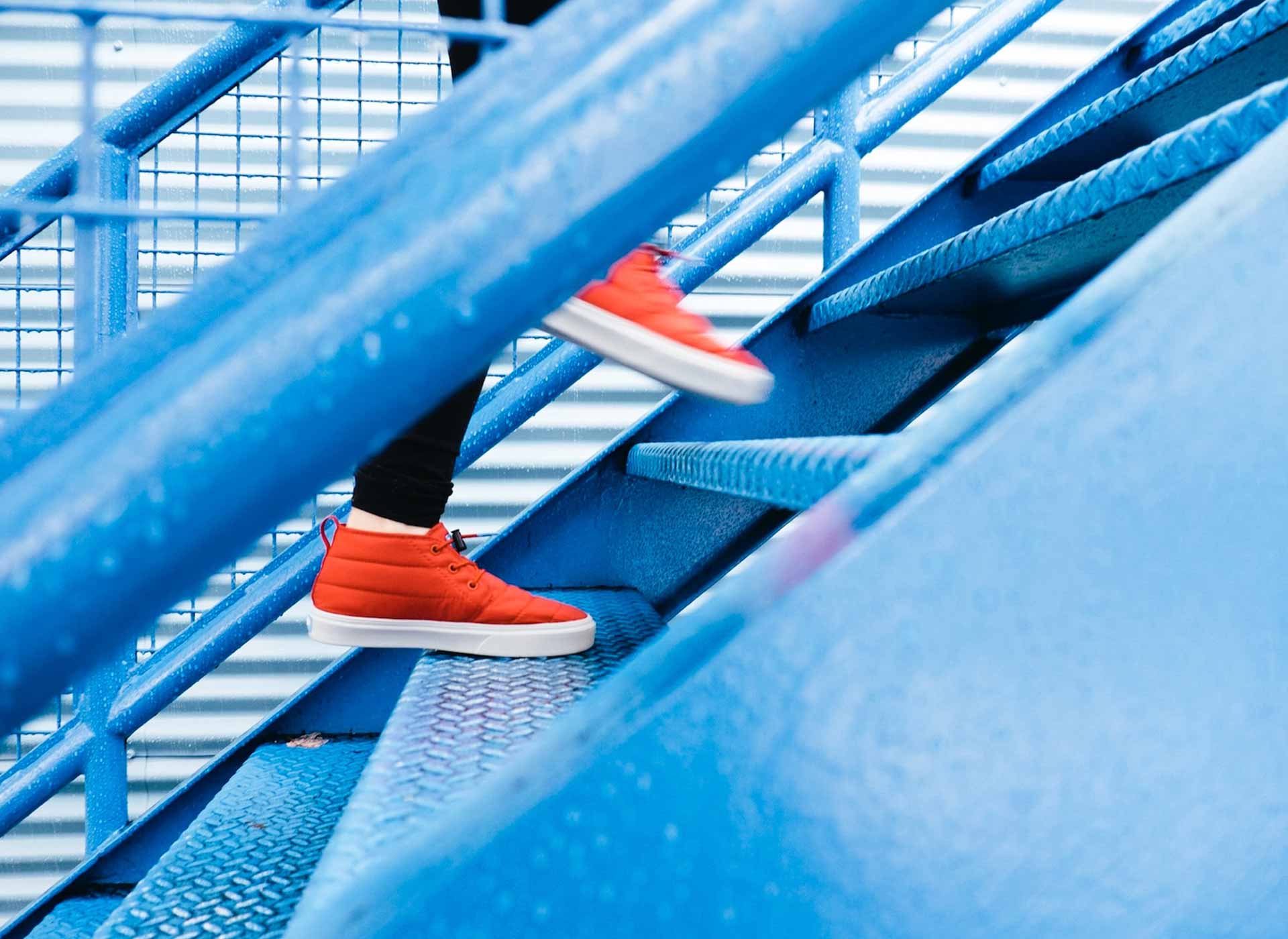 a cropped photo of a pair of orange sneakers climbing a set of stairs